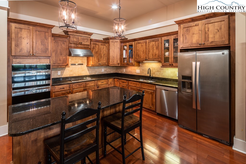 a kitchen with stainless steel appliances granite countertop a refrigerator a sink dishwasher a stove and white countertops with wooden floor