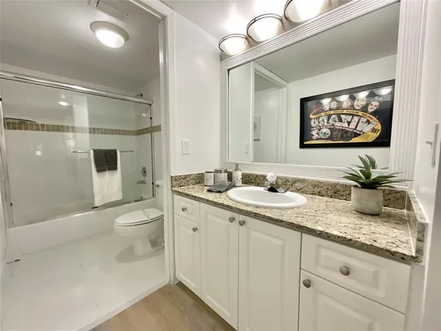 a bathroom with a granite countertop sink a toilet a mirror and shower
