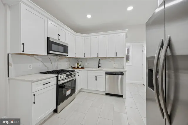 a kitchen with stainless steel appliances granite countertop a refrigerator a stove a sink and white cabinets