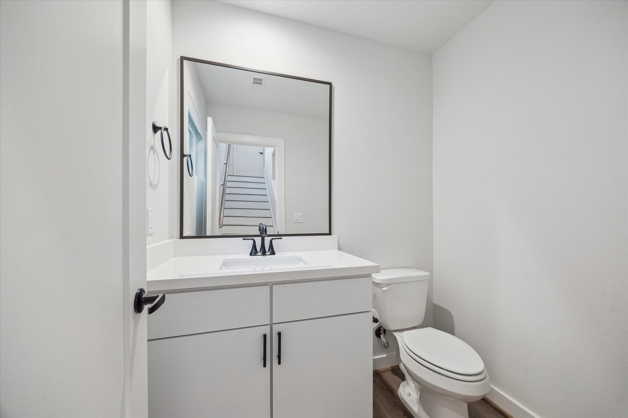 1603 Patterson Street, Unit E Houston, TX 77007 - Photo 10 of 32 This photo shows a modern, minimalist bathroom with a white vanity, large mirror, and a toilet. The neutral tones and sleek fixtures create a clean, bright atmosphere.