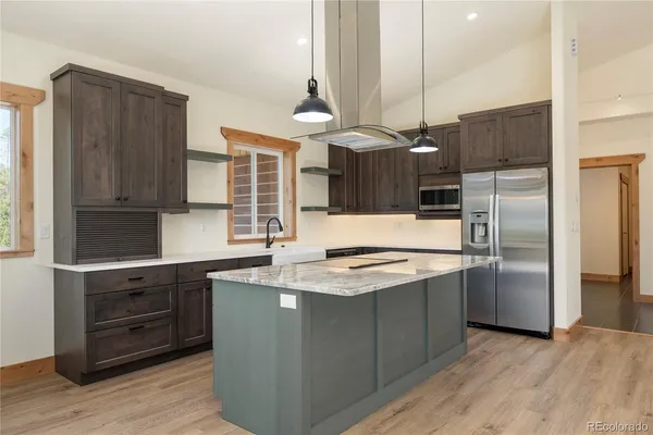 a kitchen with stainless steel appliances granite countertop a sink a stove a refrigerator and island with wooden floor