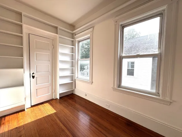 an empty room with wooden floor cabinet and windows