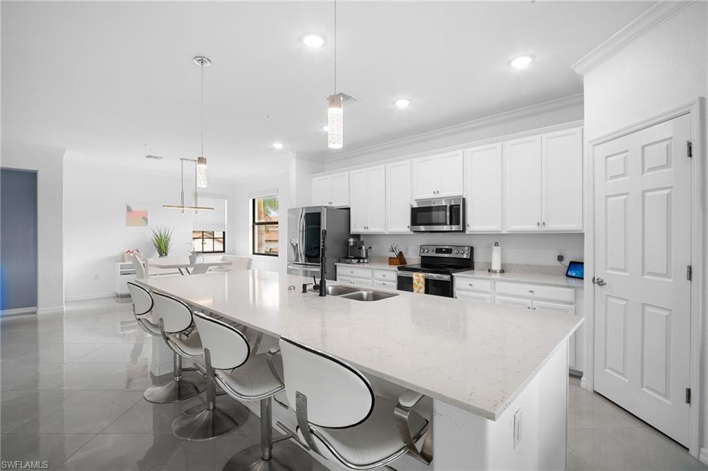 11879 Arboretum Run Drive, Unit 201 Fort Myers, FL 33913 - Photo 11 of 37 Kitchen featuring a breakfast bar area, white cabinets, hanging light fixtures, a large island, and crown molding