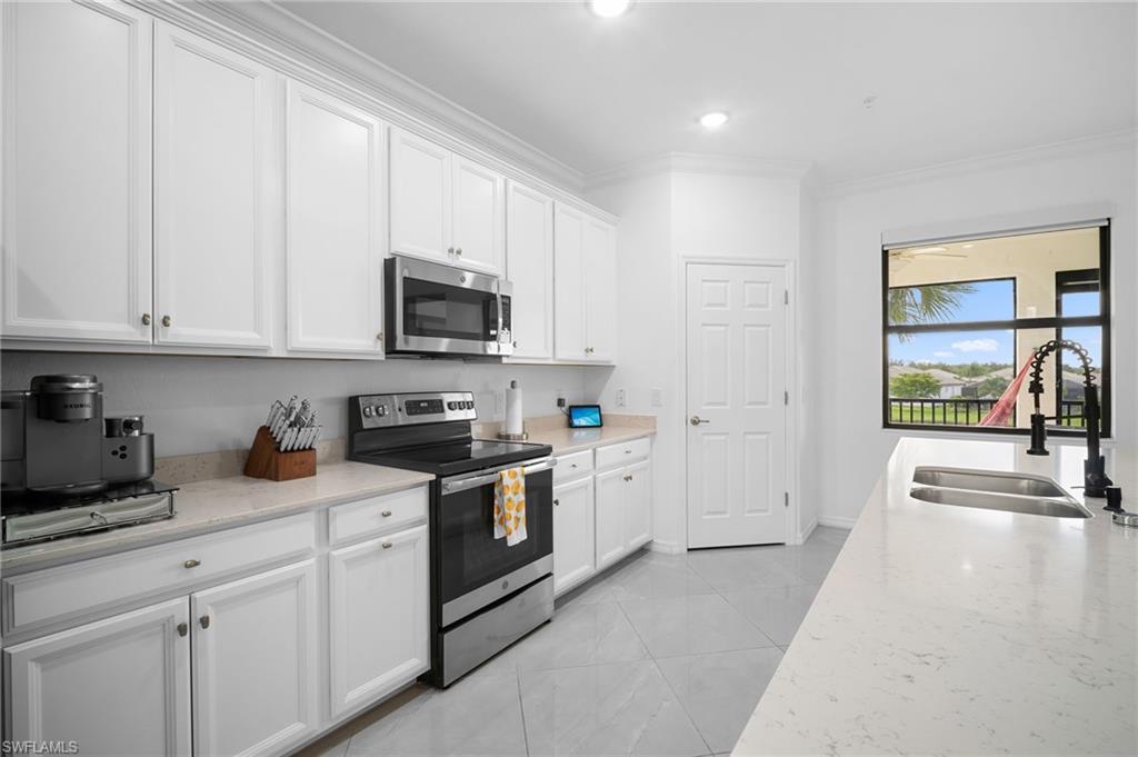 11879 Arboretum Run Drive, Unit 201 Fort Myers, FL 33913 - Photo 13 of 37 Kitchen featuring stainless steel appliances, crown molding, white cabinets, light stone counters, and light tile patterned floors