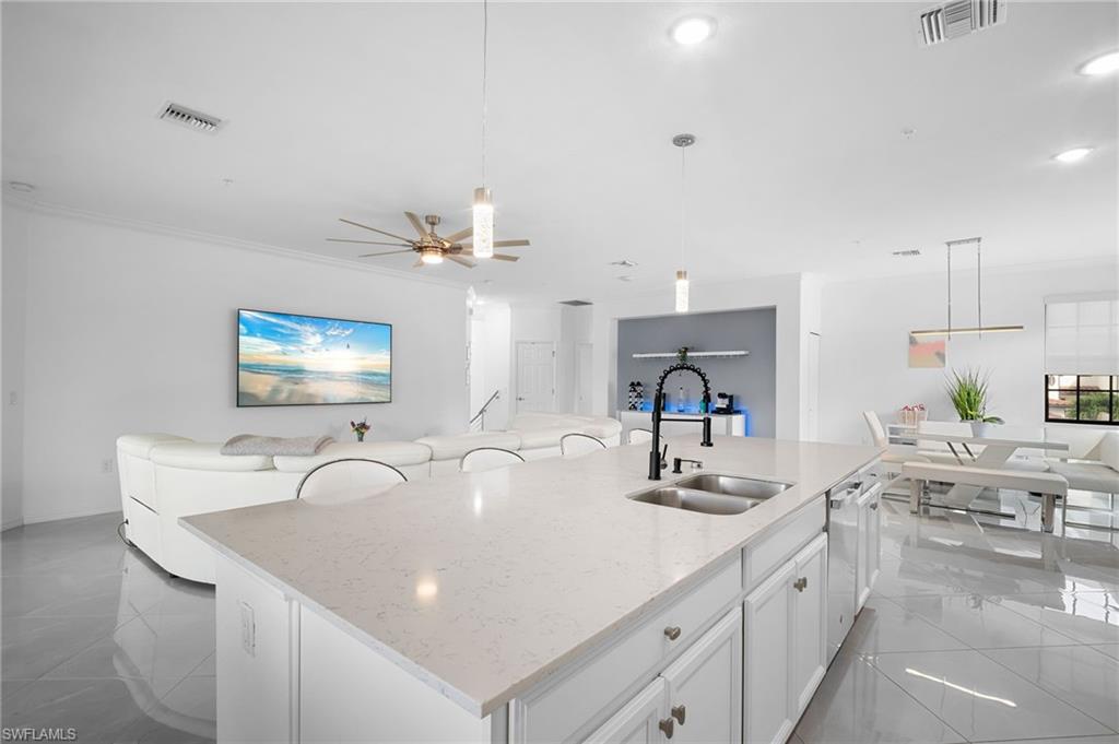11879 Arboretum Run Drive, Unit 201 Fort Myers, FL 33913 - Photo 15 of 37 Kitchen featuring white cabinetry, hanging light fixtures, open floor plan, an island with sink, and light stone counters