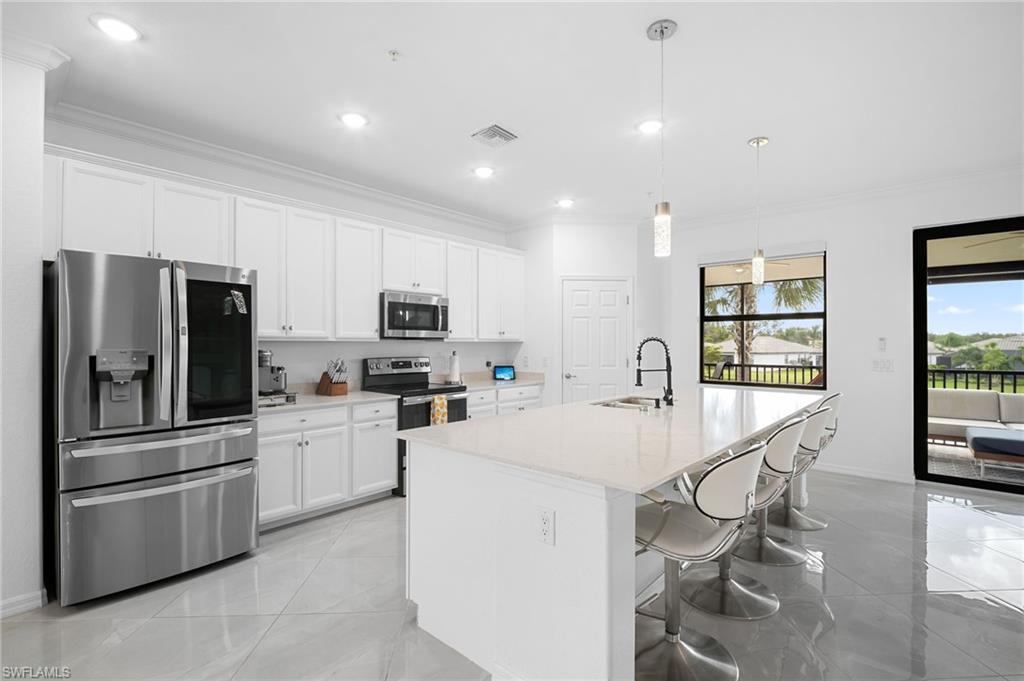 11879 Arboretum Run Drive, Unit 201 Fort Myers, FL 33913 - Photo 10 of 37 Kitchen with crown molding, stainless steel appliances, a kitchen bar, white cabinets, and pendant lighting