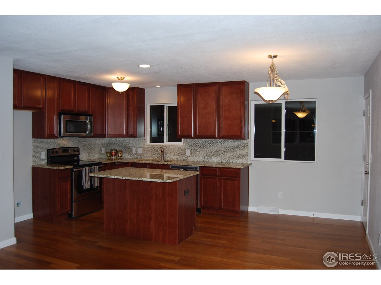 10747 Routt Street Westminster, CO 80021 - Photo 3 of 10 a kitchen with kitchen island granite countertop wooden floors wooden cabinets a refrigerator and a sink