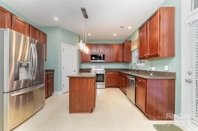 a open kitchen with stainless steel appliances granite countertop a refrigerator a sink dishwasher a stove top oven a large island with wooden cabinets and floor