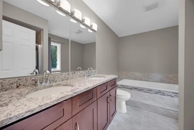 a bathroom with a granite countertop sink a toilet a mirror and bathtub
