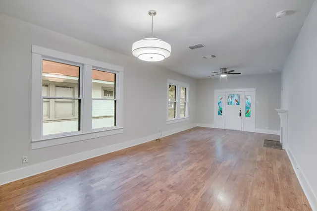 an empty room with wooden floor a ceiling fan and windows