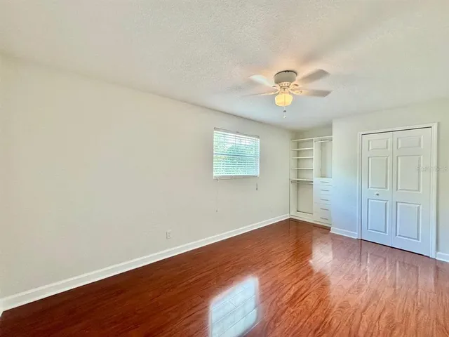 an empty room with wooden floor and a ceiling fan