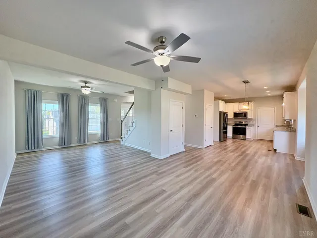 a view of an empty room with wooden floor and a ceiling fan