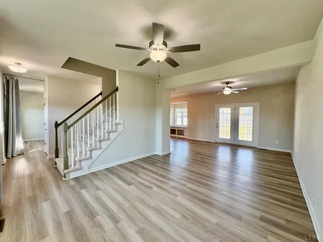 an empty room with wooden floor chandelier fan and windows