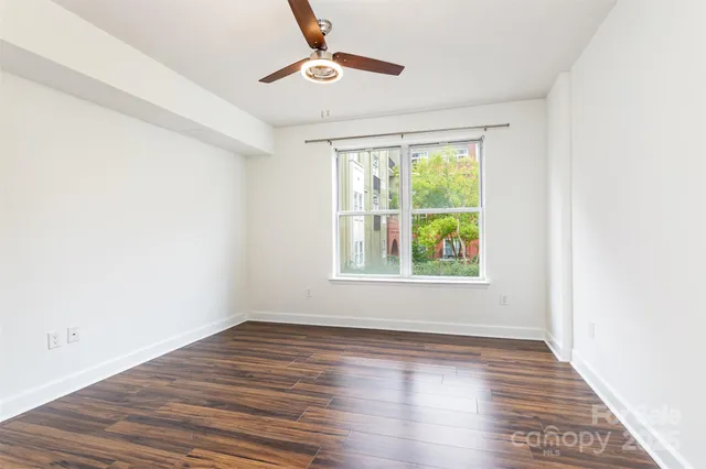 an empty room with wooden floor chandelier fan and windows