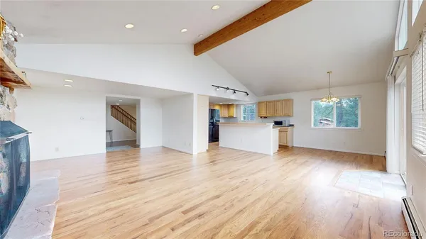 an empty room with wooden floor kitchen view and windows