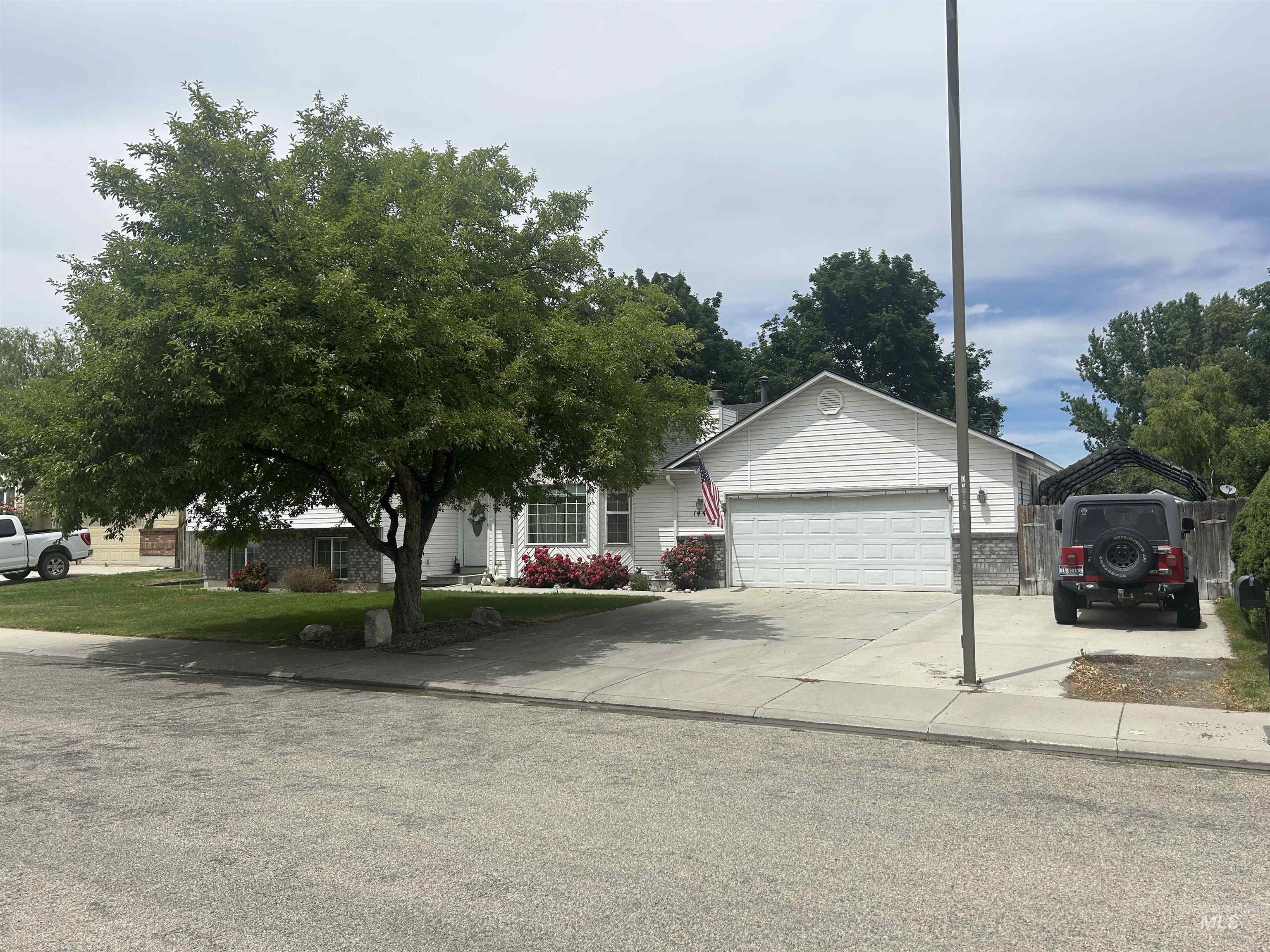 1444 East Doberman Street Meridian, ID 83642 - Photo 1 of 31 White siding exterior featuring a two-car garage, mature front yard tree, concrete driveway, and stone veneer accents
