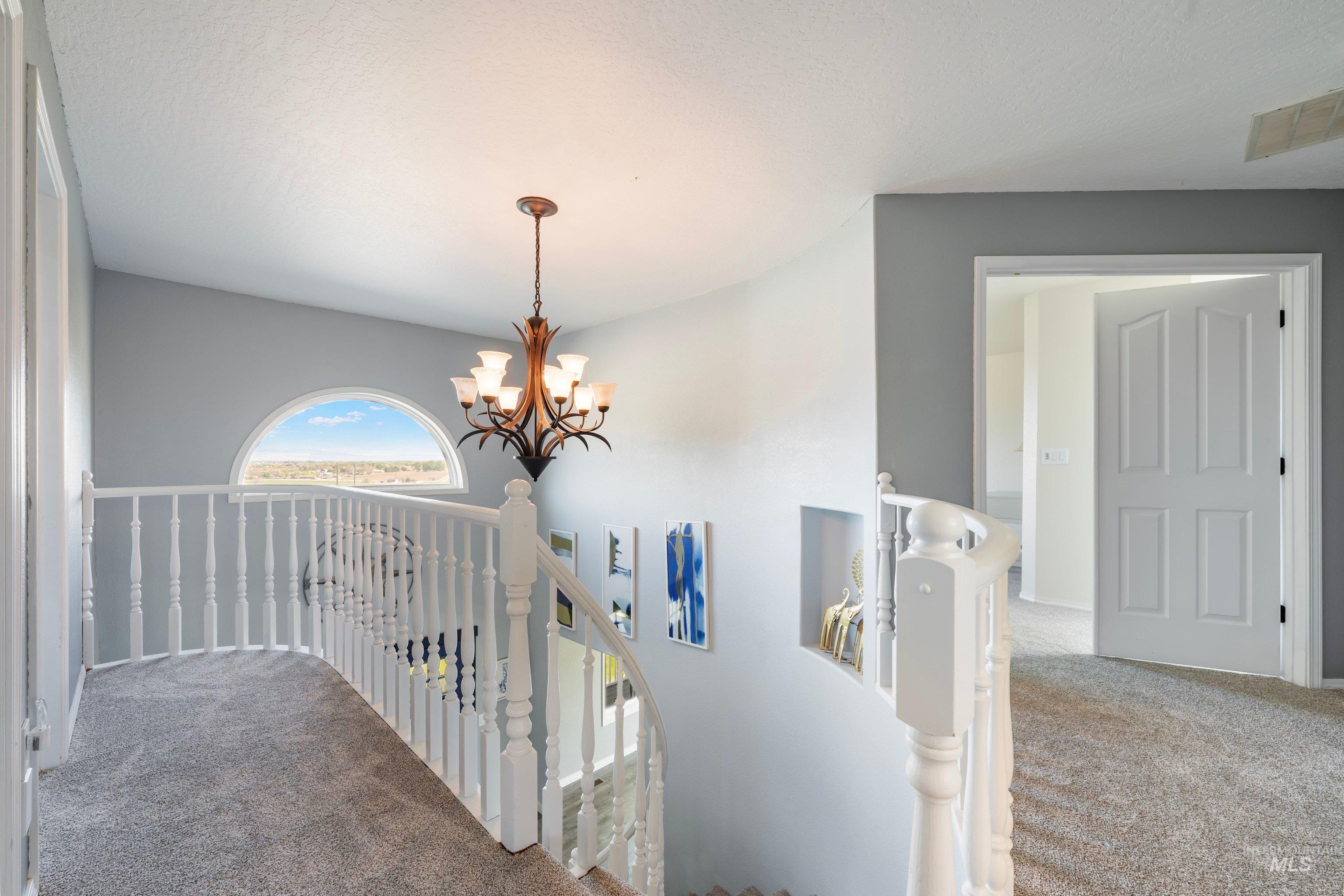 7657 Track Road Nampa, ID 83686 - Photo 20 of 49 Curved white banister with a semi-circular window, textured gray carpeting, and a wrought iron chandelier