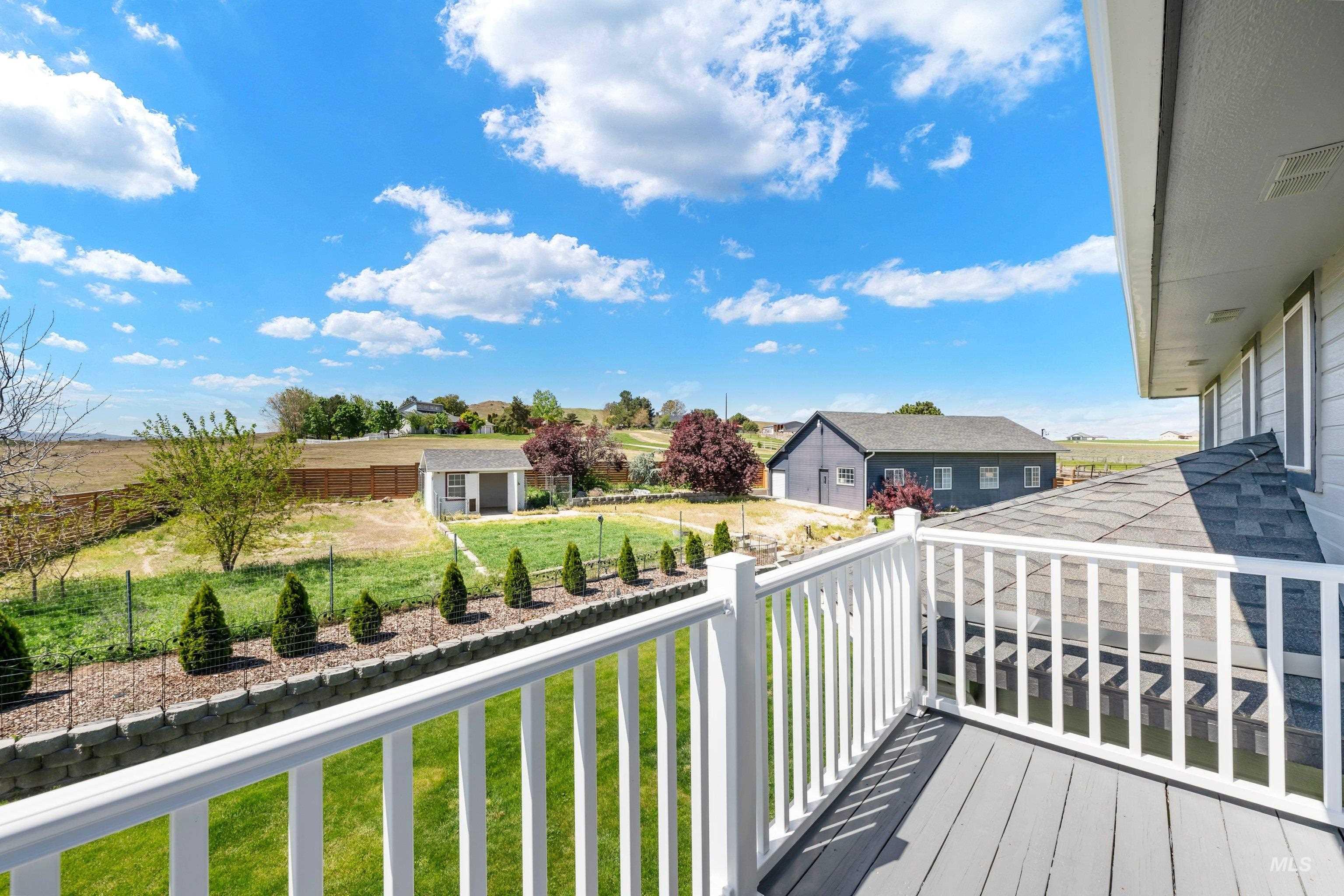 7657 Track Road Nampa, ID 83686 - Photo 27 of 49 Spacious outdoor deck with white railing overlooking a substantial green lawn, retaining wall with planted shrubs, and a detached shed