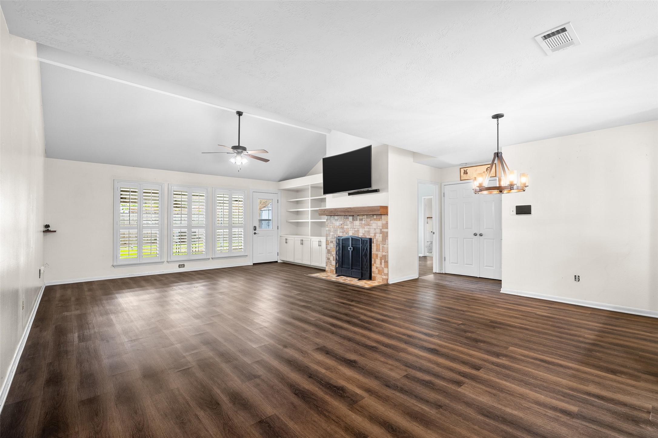 4826 Stonebridge Street Baytown, TX 77521 - Photo 2 of 18 Enjoy a bright and welcoming living room complete with classic shutters, a wood-burning fireplace, modern vinyl plank flooring, and thoughtfully designed built-in cabinets and shelves ideal for storage and display.