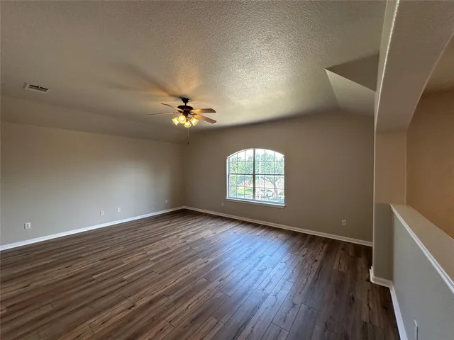 an empty room with wooden floor chandelier fan and windows