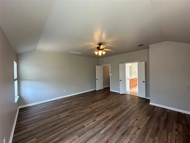 an empty room with wooden floor chandelier fan and windows