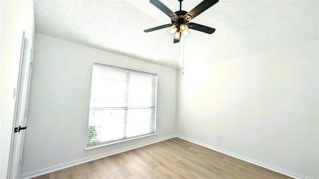 an empty room with wooden floor fan and windows