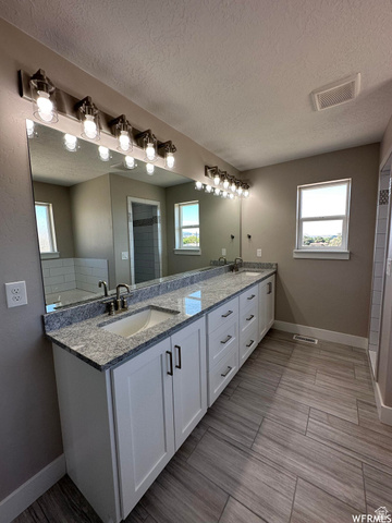 1171 West 2330 North Helper, UT 84526 - Photo 15 of 26 Bathroom featuring double vanity, a textured ceiling, tiled shower, and wood finish floors
