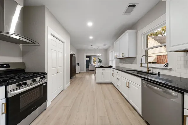 a large kitchen with stainless steel appliances granite countertop a stove top oven a sink dishwasher a refrigerator and white cabinets with wooden floor