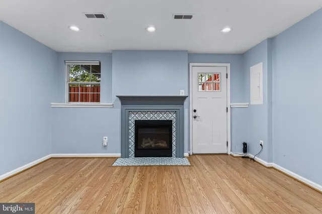 a view of an empty room with wooden floor fireplace and a window