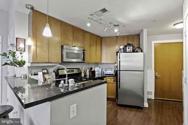 a kitchen with stainless steel appliances granite countertop a refrigerator a sink a stove a microwave a counter space and wooden floor