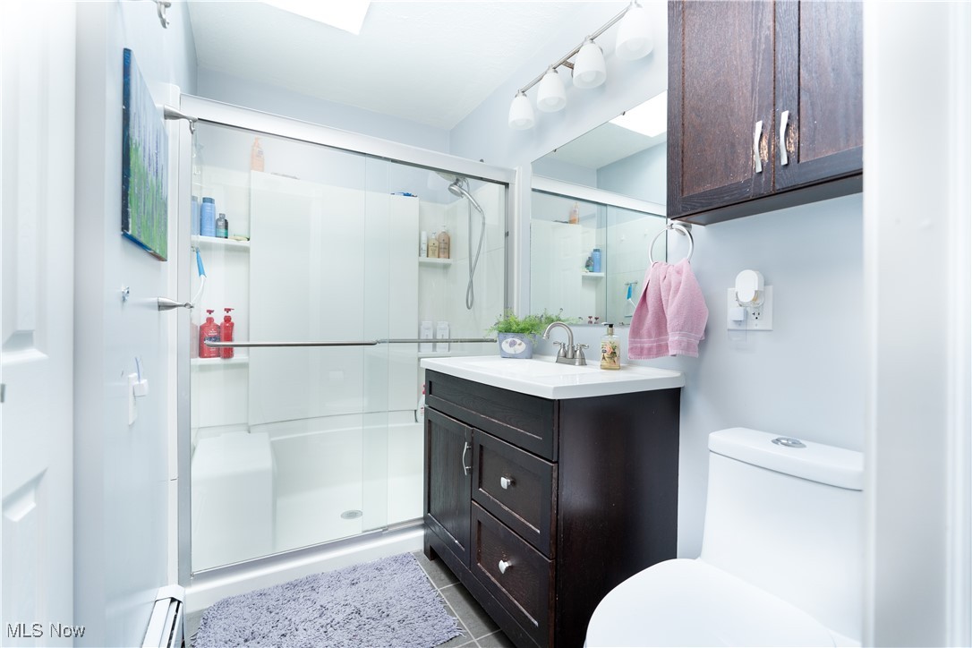 Bathroom featuring a shower with door, vanity, tile patterned flooring, and toilet