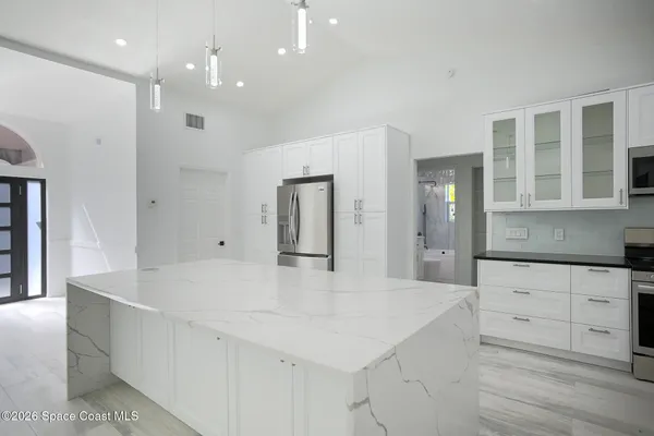 a large white kitchen with kitchen island a sink stainless steel appliances and cabinets