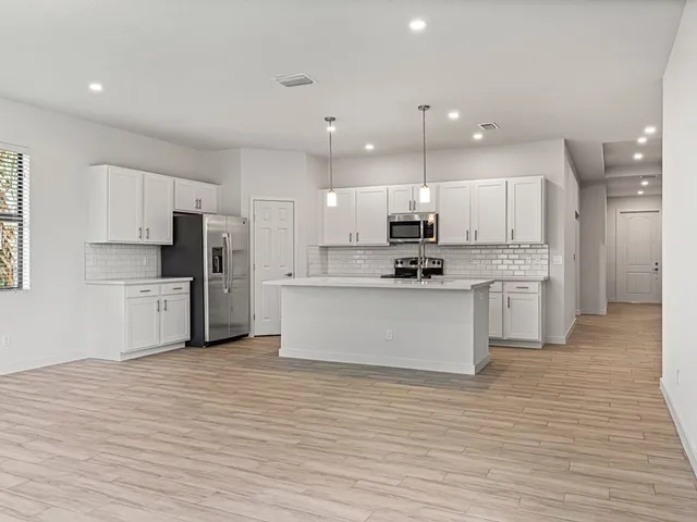 a large kitchen with stainless steel appliances kitchen island granite countertop a stove a sink a refrigerator and white cabinets with wooden floor