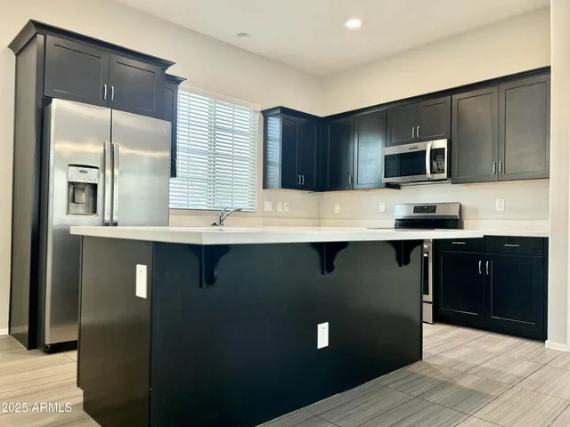 a kitchen with stainless steel appliances kitchen island granite countertop a refrigerator a stove top oven and a sink with wooden floor