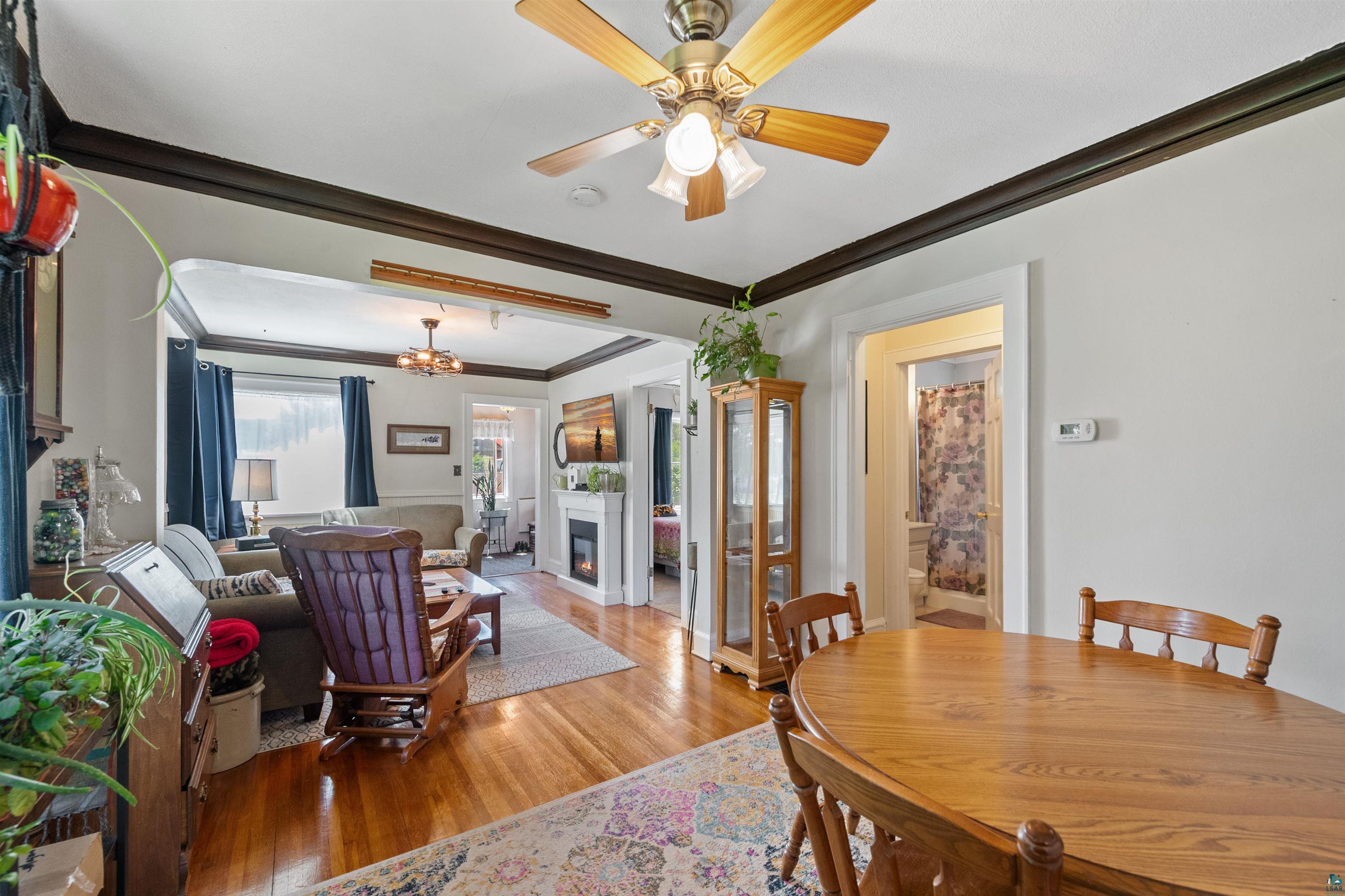 3209 Chestnut Street Duluth, MN 55806 - Photo 8 of 28 Spacious dining area with a natural wood-finish table and chairs, featuring wood-finish flooring, a ceiling fan with integrated lighting, and an entryway to an adjoining room with a fireplace