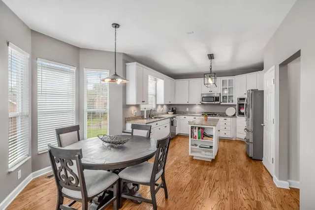 a kitchen with stainless steel appliances kitchen island granite countertop a dining table chairs and white cabinets