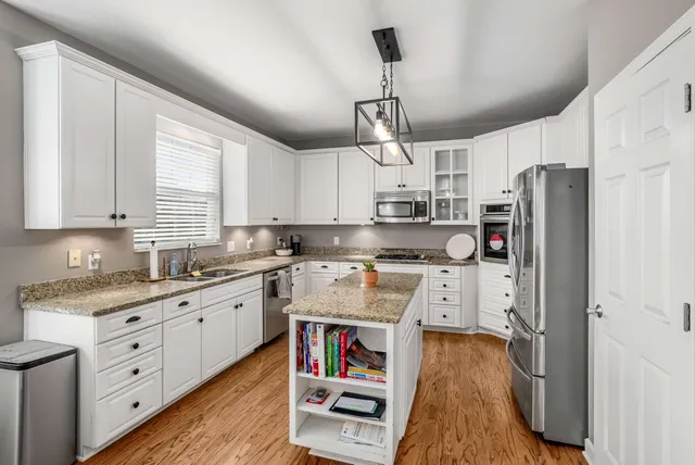 a kitchen with stainless steel appliances granite countertop a refrigerator a sink dishwasher a stove and white cabinets with wooden floor