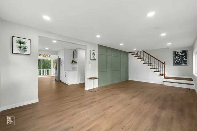 a view of an empty room with wooden floor and a kitchen