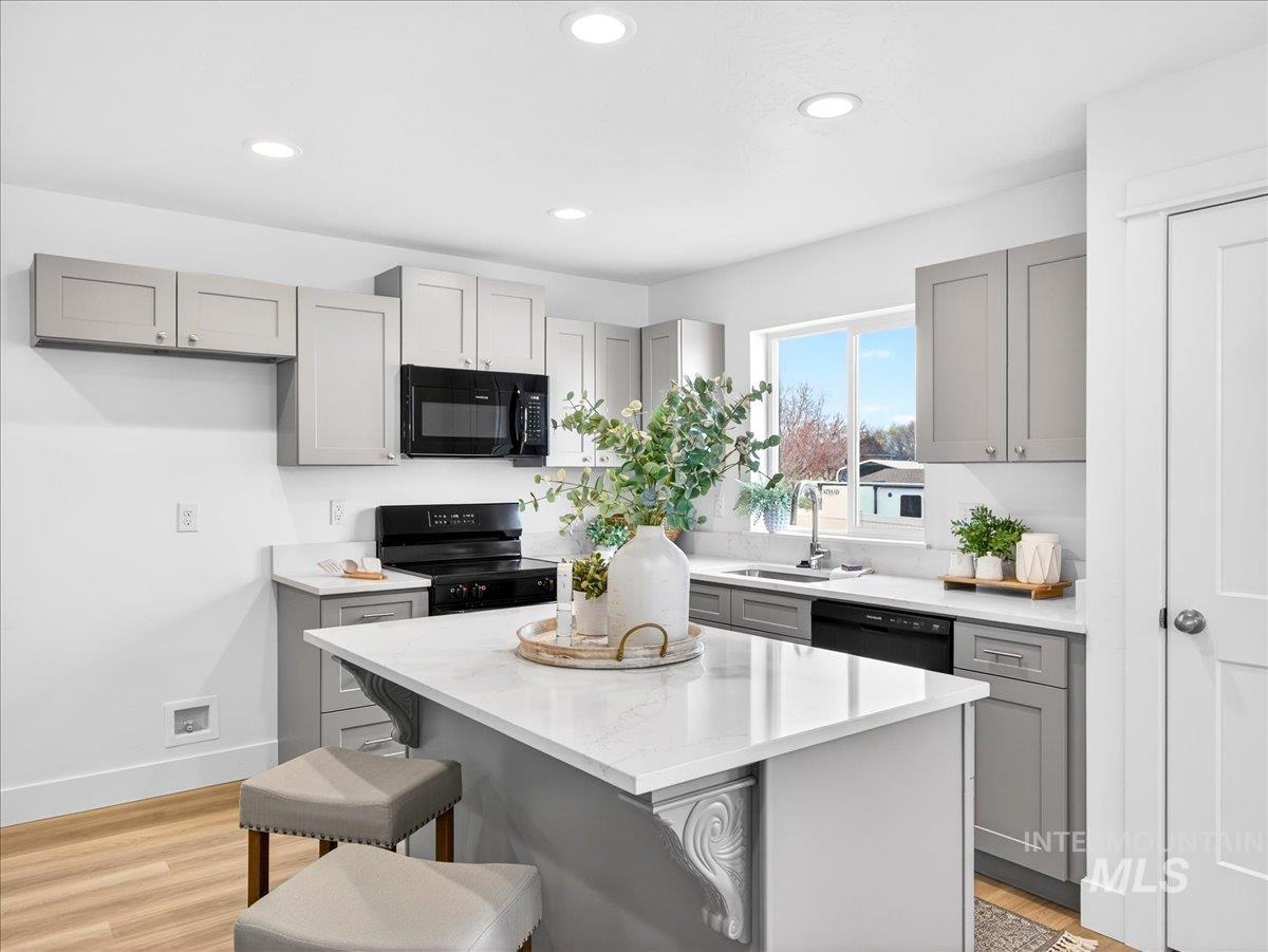 1611 Regency Way Emmett, ID 83617 - Photo 15 of 47 Kitchen featuring gray cabinetry, a kitchen breakfast bar, black appliances, a center island, and light wood-type flooring