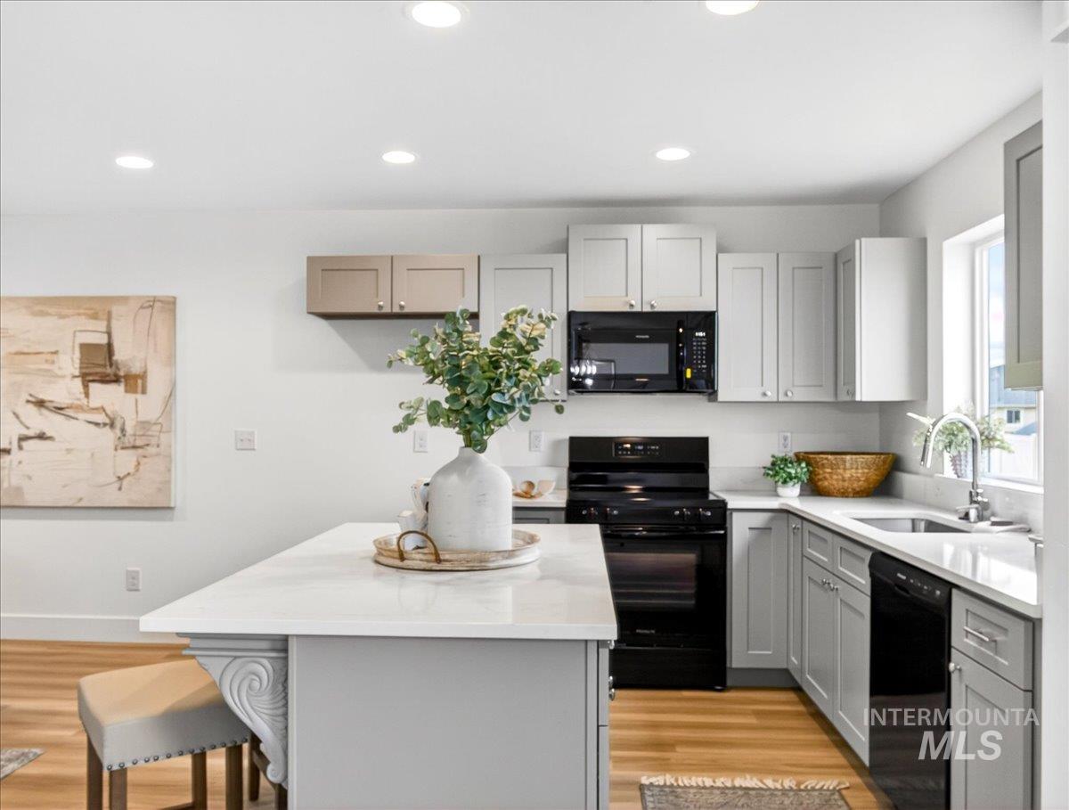 1611 Regency Way Emmett, ID 83617 - Photo 17 of 47 Kitchen featuring black appliances, gray cabinetry, light wood-style floors, light stone countertops, and a kitchen island