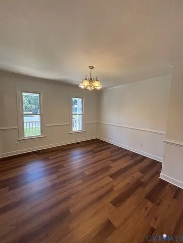an empty room with wooden floor chandelier and windows