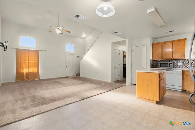 a view of an empty room and kitchen with a ceiling fan