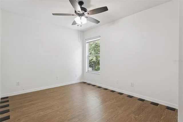 an empty room with wooden floor fan and windows