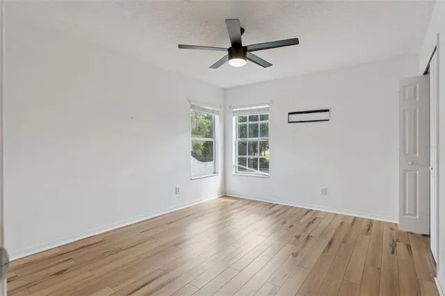 an empty room with wooden floor fan and windows