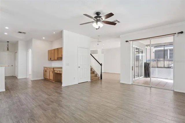 a view of an empty room with wooden floor and a ceiling fan