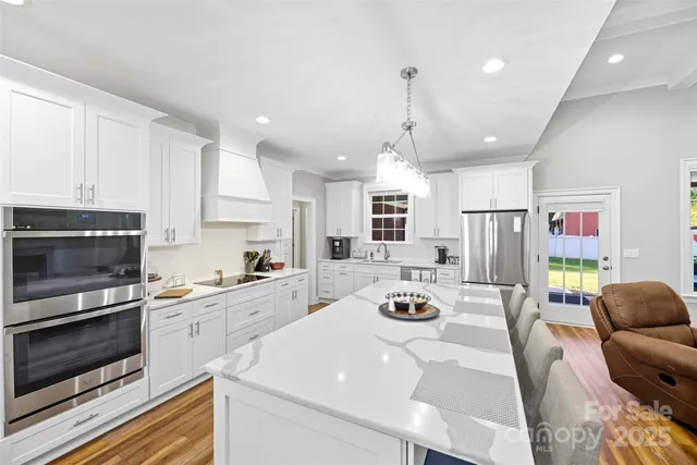 a kitchen with stainless steel appliances a stove a sink dishwasher a refrigerator white cabinets and couches with wooden floor