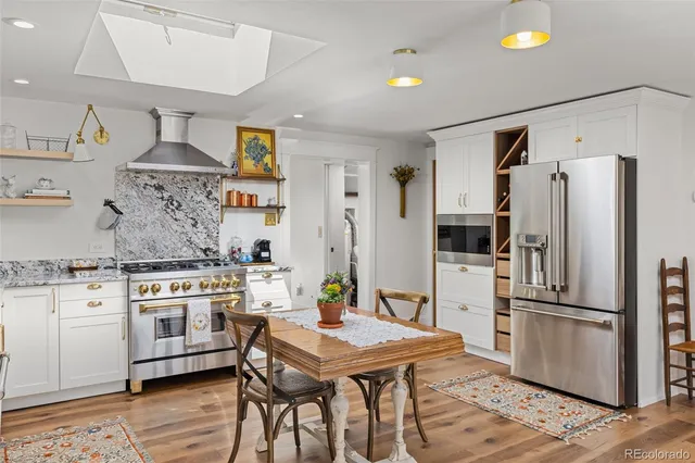 a kitchen with stainless steel appliances a stove a refrigerator and a dining table with wooden floor