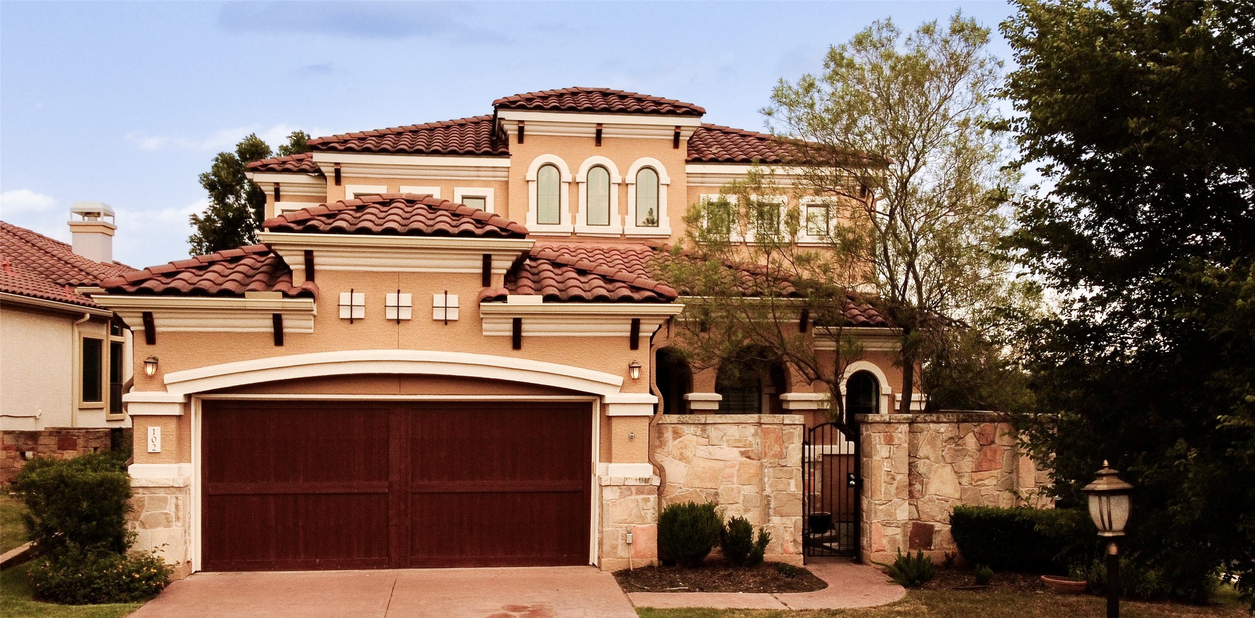 Mediterranean / spanish-style home with a gate, stone siding, a tile roof, driveway, and stucco siding