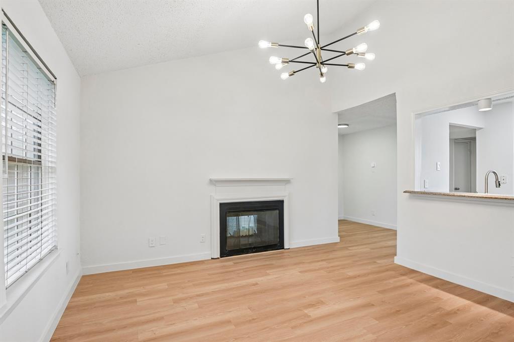 5300 Keller Springs Road, Unit 2055 Dallas, TX 75248 - Photo 1 of 24 Spacious living area featuring a vaulted ceiling with a contemporary sputnik chandelier, wood-finish flooring, and a fireplace with a classic white mantel