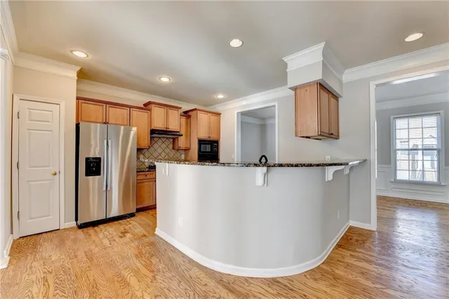 a view of kitchen with stainless steel appliances granite countertop a refrigerator a sink a stove and white cabinets with wooden floor